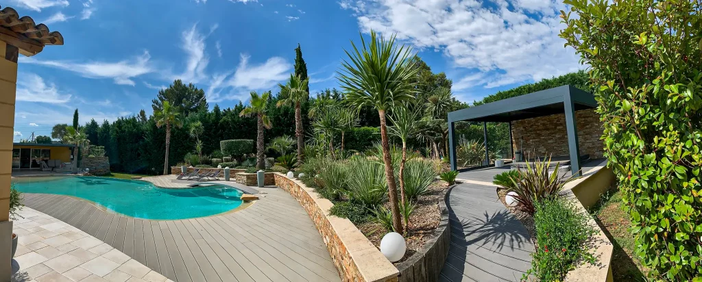 Aménagement paysager panoramique d'un espace piscine à Bouc-Bel-Air, avec terrasse en lames de bois composite, mur en pierres sèches et pergola design.